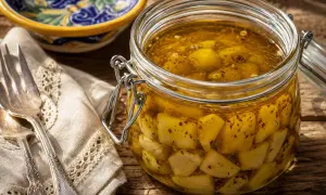 Un barattolo di aglio sott'olio, pronto per essere usato in ogni ricetta. Accanto, una forchetta e un tovagliolo ricamato.