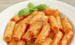 Un piatto di rigatoni al sugo, conditi con erbe aromatiche e guarniti con foglie di basilico fresco. Il maccarone, nella sua semplicità, racchiude un significato di convivialità e tradizione.