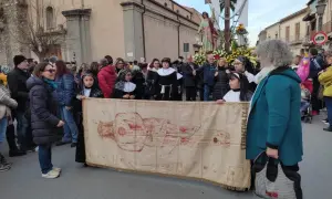 Processione con il telo della Veronica, raffigurante Cristo, tra la folla e una statua lignea.