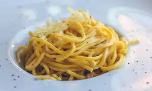 Maccheroni alla chitarra molisani, un piatto di pasta fresca condita con formaggio grattugiato e pepe nero, serviti in un piatto bianco.