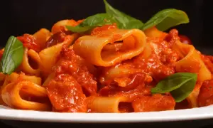 Un piatto di rigatoni allo scarpariello, conditi con un sugo rosso ricco e guarniti con foglie di basilico fresco.