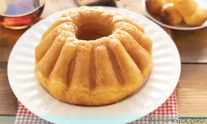 Un soffice babà, pronto per essere inzuppato, evoca la **babà ricetta originale**. Accanto, un bicchierino di rum e altri babà in miniatura.