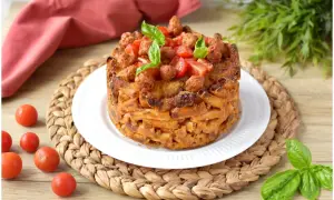Un invitante pasta timbale, dorato e ripieno, guarnito con pomodorini e basilico fresco.