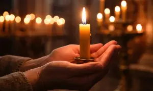 Mani che sorreggono una candela accesa, un momento di pace quando si accende la candela della candelora, con altre luci soffuse sullo sfondo.