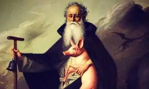 Un anziano barbuto con un maialino rosa, un bastone con campana e un'ombra di drago. La storia del porcellino di Sant'Antonio.