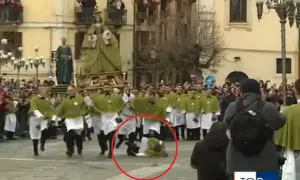 Durante una processione, un uomo cade a terra, quasi come una **madonna che scappa**, mentre altri partecipano con vesti verdi e bianche.