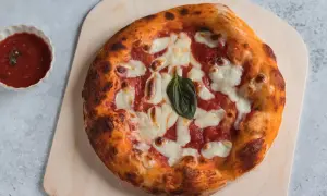 Pizza margherita appena sfornata, con crosta dorata e mozzarella filante. Accanto, una ciotolina di salsa di pomodoro, perfetta per chi ama la pizzelle ricetta tradizionale.