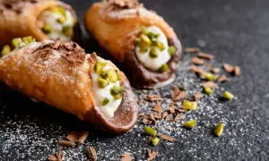 Cannoli siciliani ricetta della nonna: croccanti cialde ripiene di crema, guarnite con pistacchi e scaglie di cioccolato.