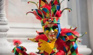 Un personaggio con un elaborato tipo di maschera di carnevale, colorato e festoso, con un cappello a punta e guanti gialli.