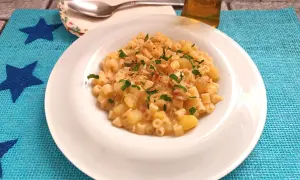 Un piatto di pasta e patate con provola filante, guarnito con prezzemolo fresco e un pizzico di peperoncino.