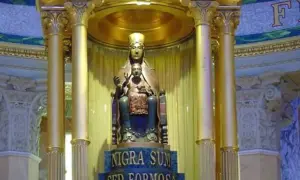 Statua dorata di una Maria nera con Gesù Bambino, su un piedistallo con iscrizione latina.