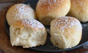 Cinque soffici panini spolverati di zucchero a velo, uno è stato morso rivelando la sua brioche rustica morbidissima.