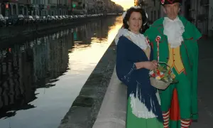 Coppia in costume tradizionale, una maschera milanese, passeggia lungo un naviglio al tramonto.