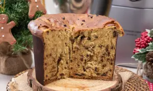 Un soffice panettone natalizio con gocce di cioccolato, tagliato a metà, su un tagliere di legno. Decorazioni natalizie sullo sfondo.