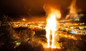 Un imponente falò illumina la notte, celebrando le glorie di San Martino. Le fiamme danzano sopra un villaggio illuminato, creando uno spettacolo magico.