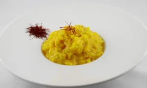 Un cremoso risotto alla milanese, giallo intenso, guarnito con pistilli di zafferano e accompagnato da una piccola porzione di zafferano essiccato.