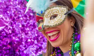 Donna sorridente con maschera di carnevale e perline colorate. L'etimologia di carnevale, "addio alla carne", si riflette nella gioia sfrenata.