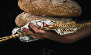 Mani che sorreggono pani rustici e spighe di grano, evocando il significato pagano del raccolto e della fertilità.