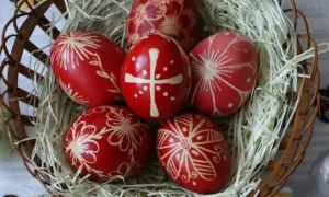 Uova di Pasqua rosse decorate con motivi floreali e una croce, simbolo uovo di Pasqua significato di rinascita e speranza, in un cesto.
