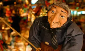 Una bambola di una strega famosa, con un naso adunco e occhi azzurri, tiene una scopa.