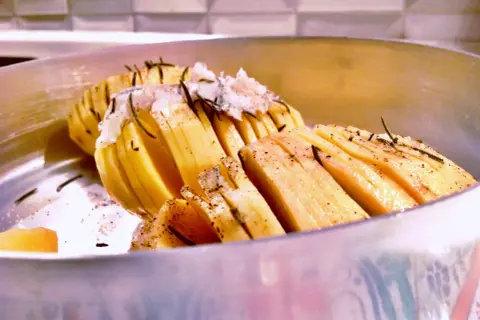Patate al coppo, tagliate a fisarmonica e condite con erbe aromatiche, pronte per essere cotte.
