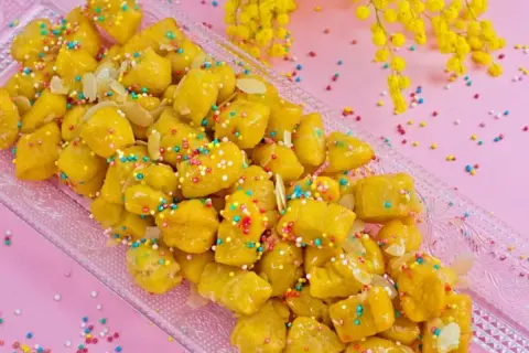 Dolcezza dorata: la ricetta cicerchiata marchigiana, decorata con confettini colorati e mandorle, pronta per essere gustata.