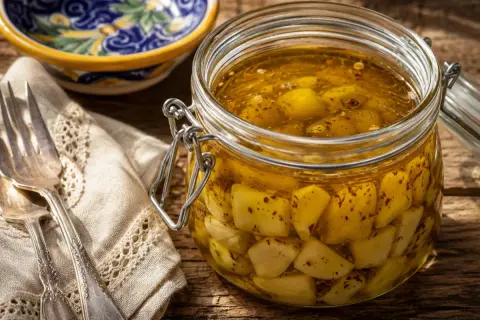 Un barattolo di aglio sott'olio, pronto per essere usato in ogni ricetta. Accanto, una forchetta e un tovagliolo ricamato.