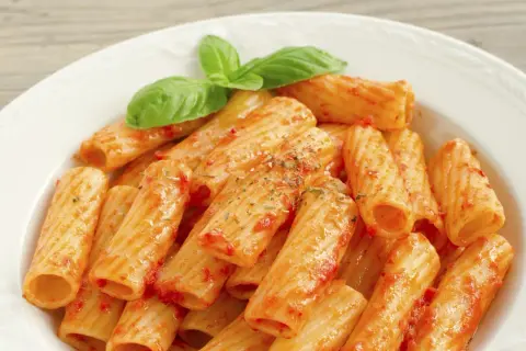 Un piatto di rigatoni al sugo, conditi con erbe aromatiche e guarniti con foglie di basilico fresco. Il maccarone, nella sua semplicità, racchiude un significato di convivialità e tradizione.