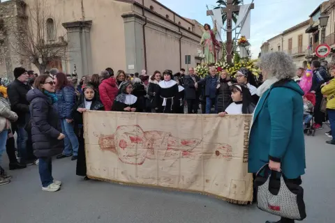 Processione con il telo della Veronica, raffigurante Cristo, tra la folla e una statua lignea.