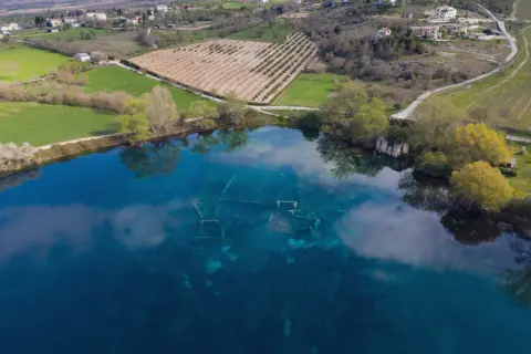 Le rovine sommerse nel lago azzurro evocano un'Atlantide d'Abruzzo. Campi verdi e alberi circondano questo luogo magico.