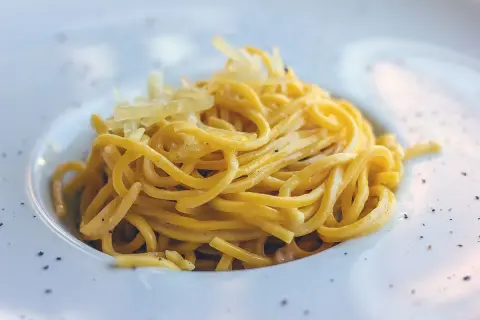 Maccheroni alla chitarra molisani, un piatto di pasta fresca condita con formaggio grattugiato e pepe nero, serviti in un piatto bianco.