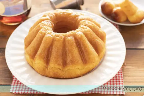 Un soffice babà, pronto per essere inzuppato, evoca la **babà ricetta originale**. Accanto, un bicchierino di rum e altri babà in miniatura.