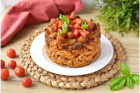 Un invitante pasta timbale, dorato e ripieno, guarnito con pomodorini e basilico fresco.
