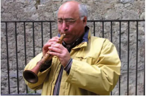 Uomo con occhiali suona uno strumento a fiato, una piva, con un suono melodioso.