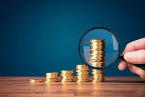 Pile di monete d'oro in crescita, esaminate da una lente d'ingrandimento. Il **regalie significato** è chiaro: l'importanza di analizzare attentamente le proprie finanze.