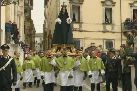 Processione a Sulmona con la Madonna che scappa, portata a spalla da uomini in verde e bianco, mentre i carabinieri sorvegliano.