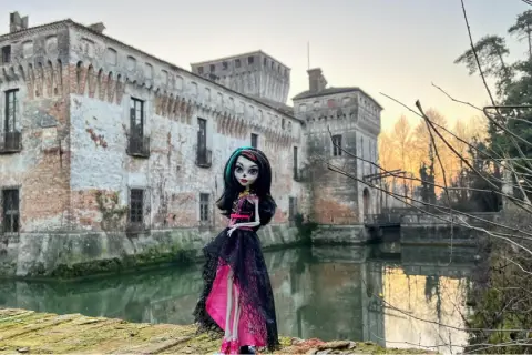 La Dama Bianca leggenda: una bambola gotica posa davanti a un castello antico con un fossato.