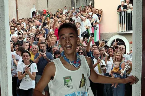 Giovane festante con la maglia "Madonna di Loreto" a Pacentro, tra una folla che filma e applaude.