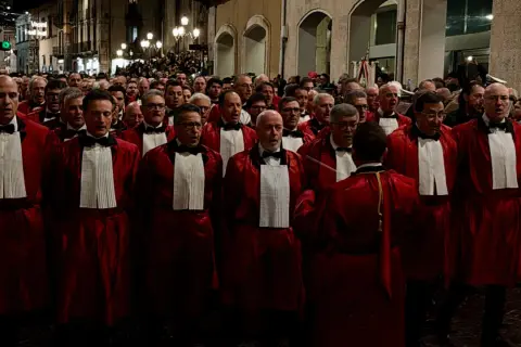 Uomini in toga rossa partecipano alla processione del Venerdì Santo a Sulmona, un momento di profonda spiritualità e tradizione.