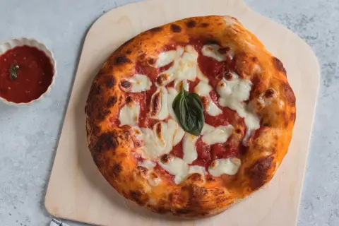 Pizza margherita appena sfornata, con crosta dorata e mozzarella filante. Accanto, una ciotolina di salsa di pomodoro, perfetta per chi ama la pizzelle ricetta tradizionale.