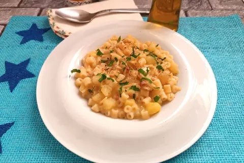 Un piatto di pasta e patate con provola filante, guarnito con prezzemolo fresco e un pizzico di peperoncino.
