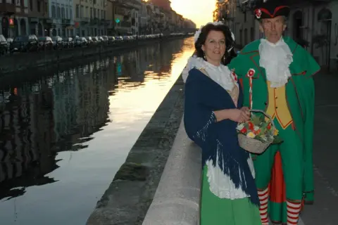 Coppia in costume tradizionale, una maschera milanese, passeggia lungo un naviglio al tramonto.
