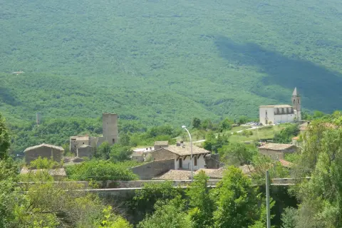 Il gigante di acciaio veglia su un borgo antico, tra torri e case di pietra, sotto un monte verdeggiante.