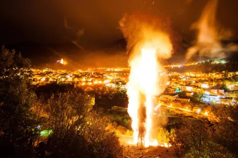 Un imponente falò illumina la notte, celebrando le glorie di San Martino. Le fiamme danzano sopra un villaggio illuminato, creando uno spettacolo magico.