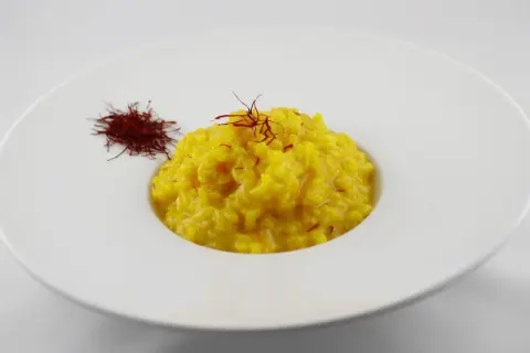 Un cremoso risotto alla milanese, giallo intenso, guarnito con pistilli di zafferano e accompagnato da una piccola porzione di zafferano essiccato.