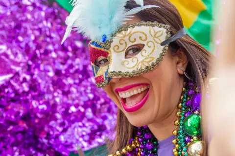 Donna sorridente con maschera di carnevale e perline colorate. L'etimologia di carnevale, "addio alla carne", si riflette nella gioia sfrenata.