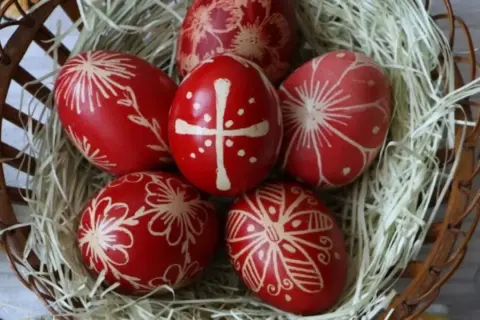 Uova di Pasqua rosse decorate con motivi floreali e una croce, simbolo uovo di Pasqua significato di rinascita e speranza, in un cesto.