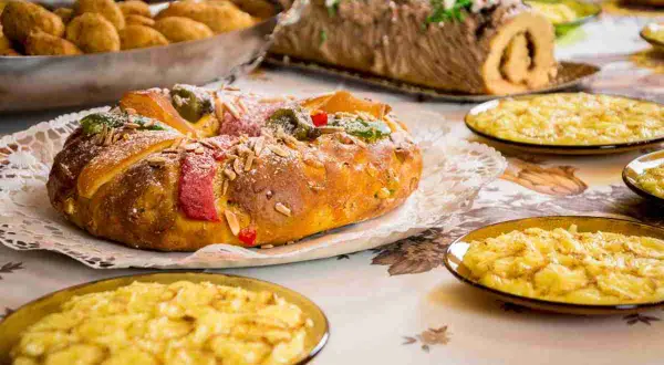 Dolce tipico dell'Epifania: un Roscón de Reyes decorato con frutta candita e mandorle, accompagnato da dolcetti.