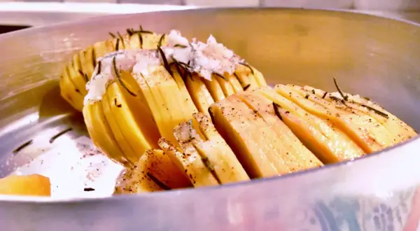 Patate al coppo, tagliate a fisarmonica e condite con erbe aromatiche, pronte per essere cotte.