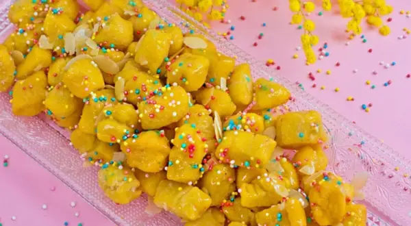 Dolcezza dorata: la ricetta cicerchiata marchigiana, decorata con confettini colorati e mandorle, pronta per essere gustata.